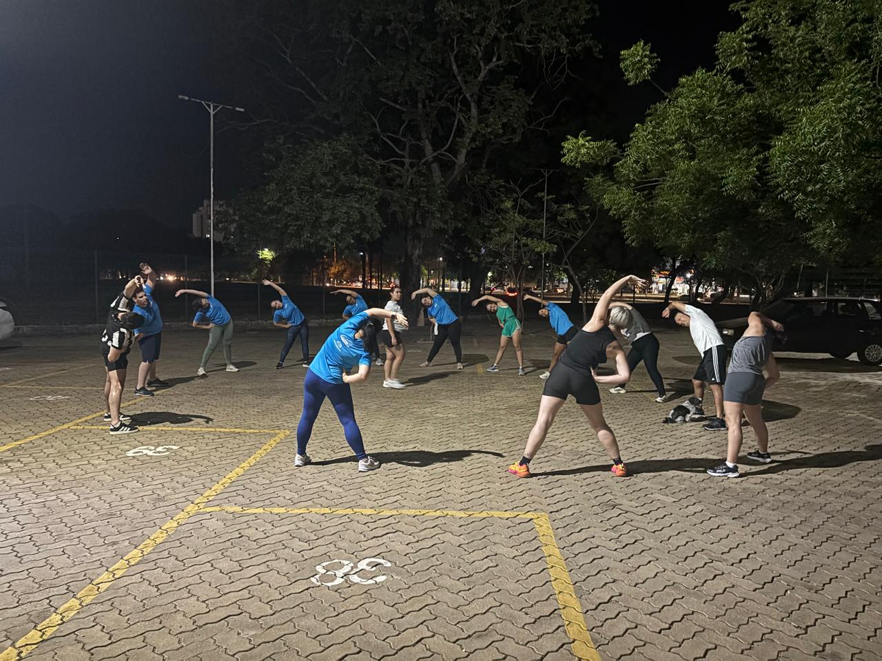 Participantes do projeto Judiciário na Medida realizam exercícios de alongamento em grupo durante atividade noturna ao ar livre.