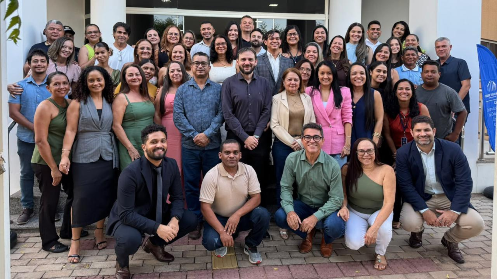 A imagem mostra um grupo de servidores e servidoras da Comarca de Araguatins reunidos em frente ao prédio do fórum, durante a homenagem ao juiz José Carlos Tajra Reis Júnior. O grupo aparece sorrindo e posando para a fotografia.
