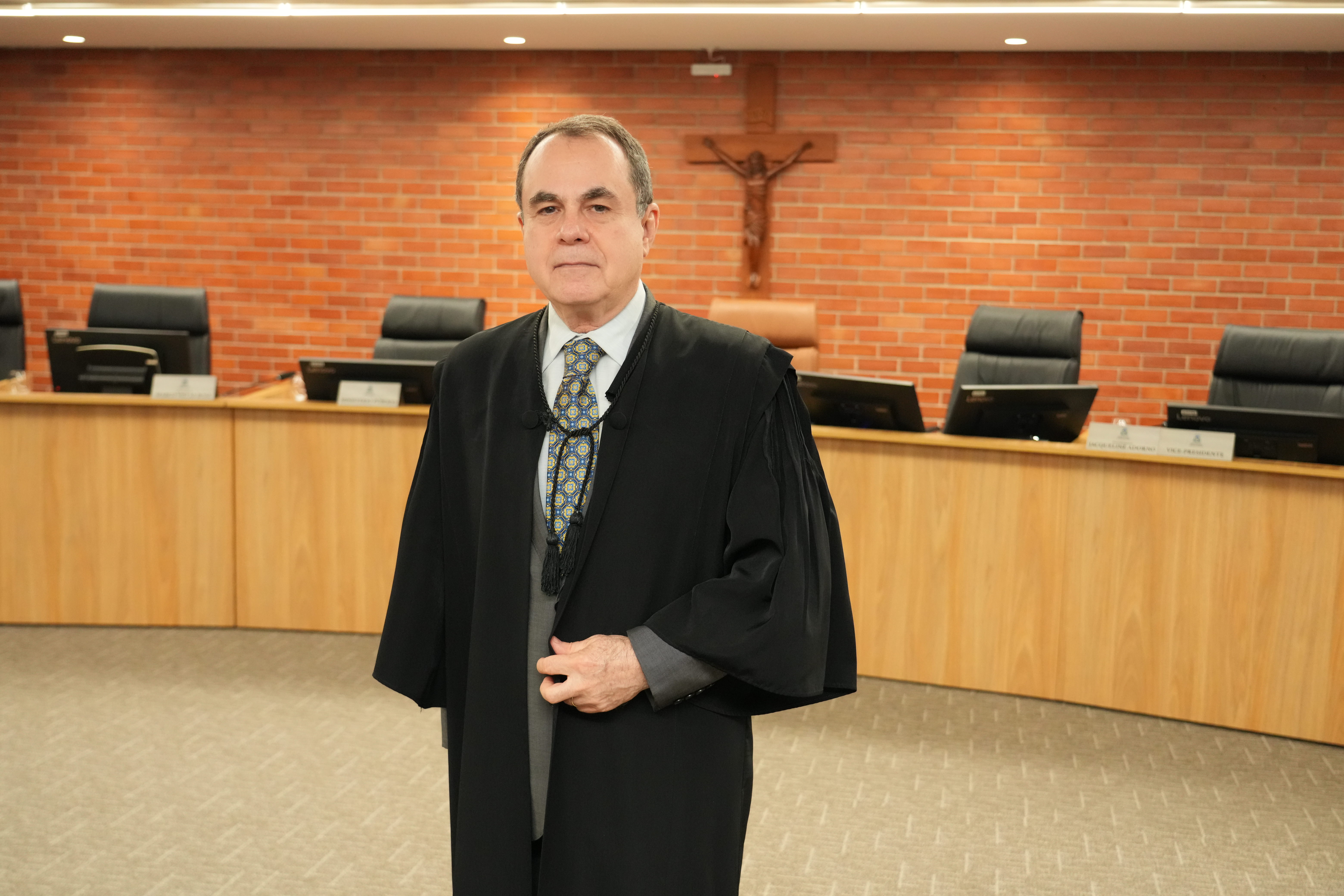 O desembargador Marco Villas Boas está em pé, no centro do plenário, vestindo toga preta sobre terno cinza e gravata estampada.
