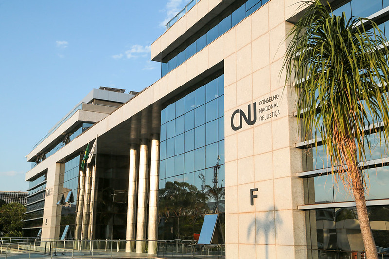 Fachada do prédio do Conselho Nacional de Justiça (CNJ), com estrutura em concreto e vidro. A sigla CNJ e o nome Conselho Nacional de Justiça aparecem na lateral do edifício.