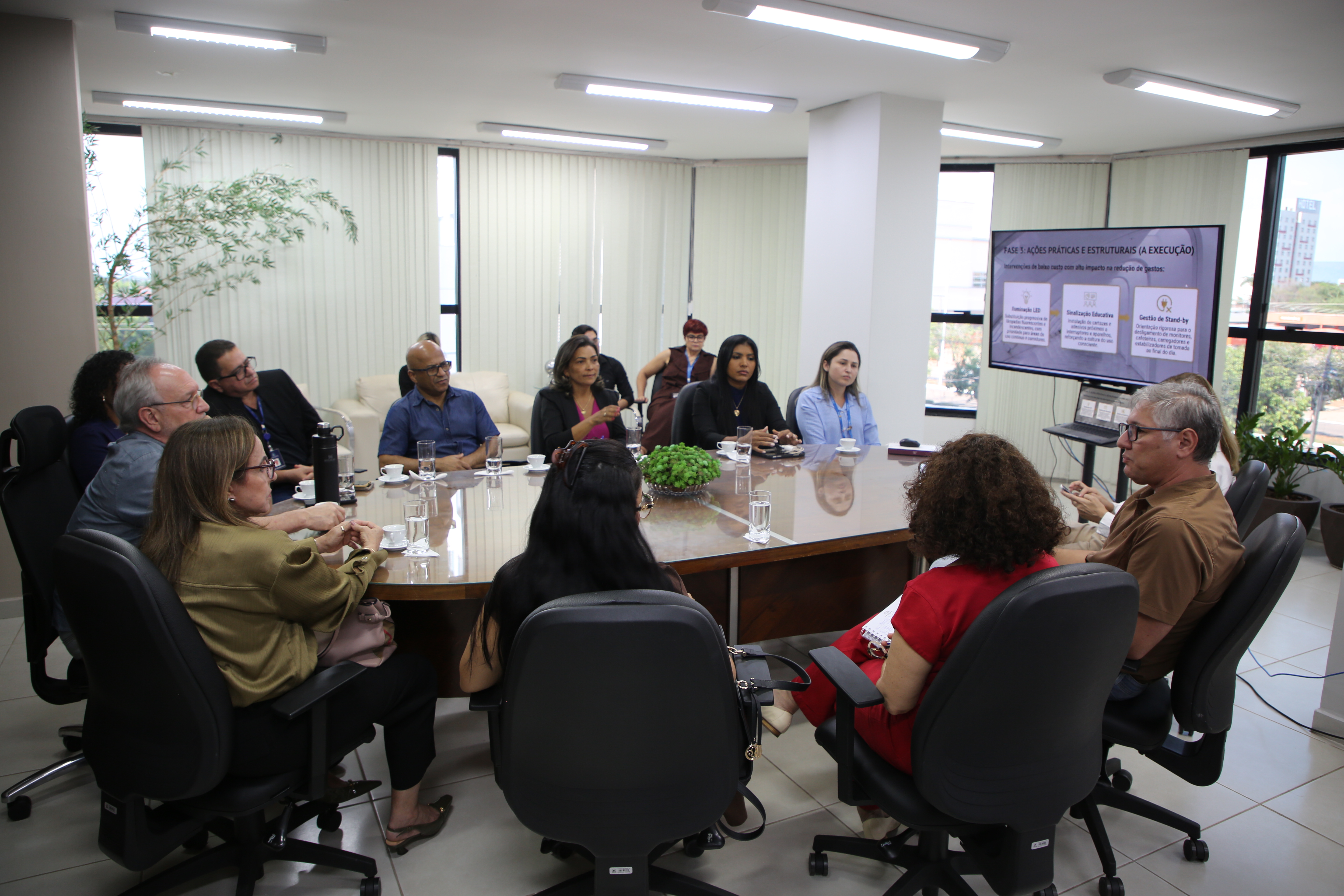 Diversos integrantes do Judiciário estão reunidos ao redor de uma grande mesa oval em uma sala iluminada durante a apresentação do projeto "Você é Luz" do Tribunal de Justiça do Tocantins a Corregedoria-Geral da Justiça do Tocantins.