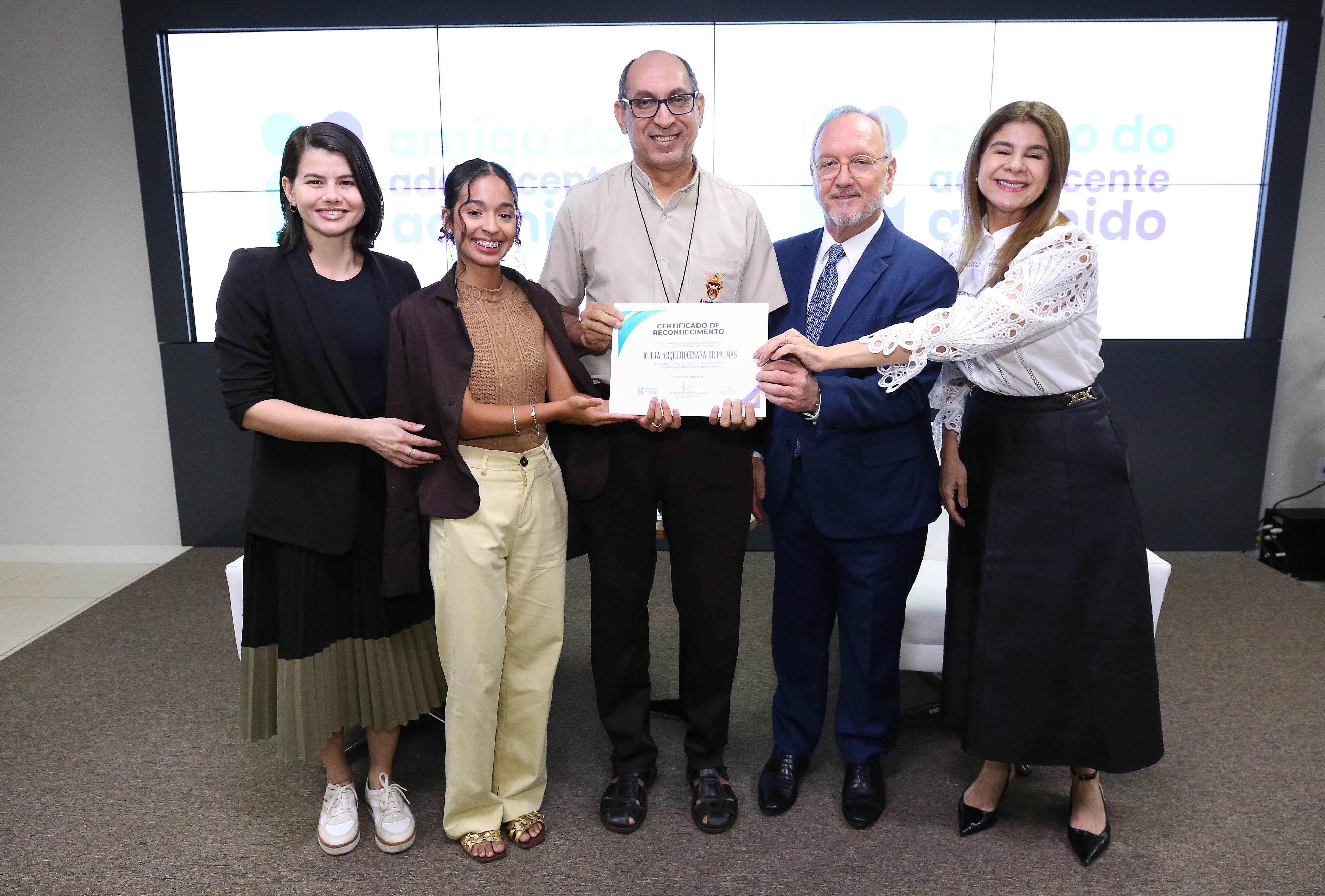 Cinco pessoas posam sorridentes em um auditório, segurando juntas o certificado 