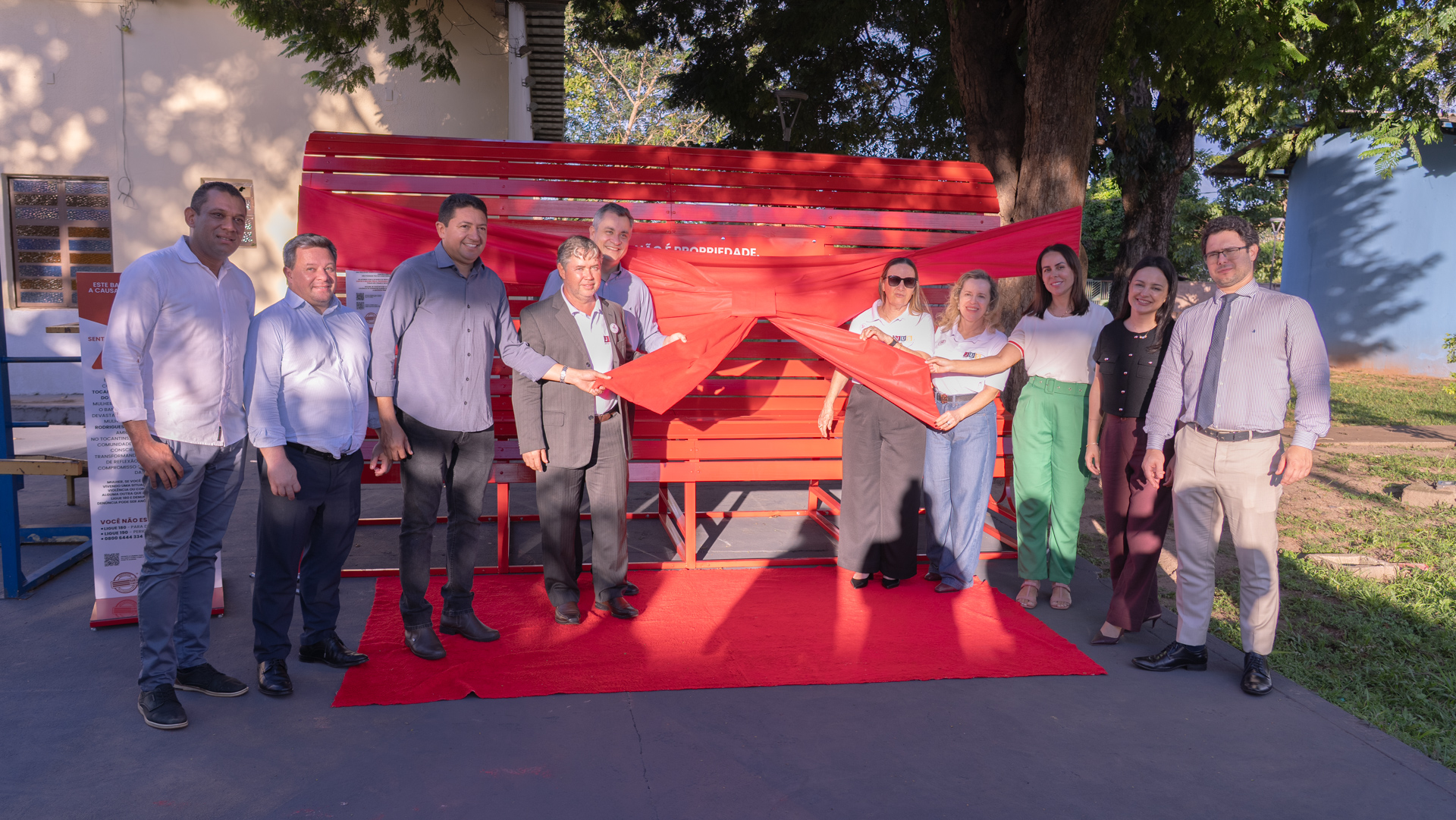 Imagem mostra diversas pessoas em frente à instalação Banco Vermelho segurando um laço de inauguração do equipamento