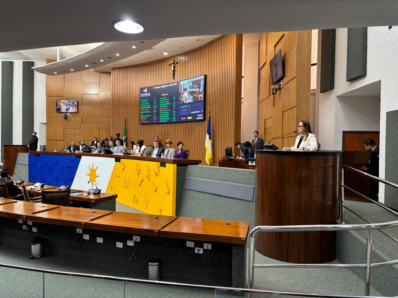 A imagem mostra o plenário da Assembleia Legislativa do Tocantins durante sessão solene da abertura do ano legislativo de 2026, com várias autoridades sentadas à mesa diretora e a presidente do TJTO, desembargadora Maysa Vendramini Rosal, utiliza a tribuna à direita. 