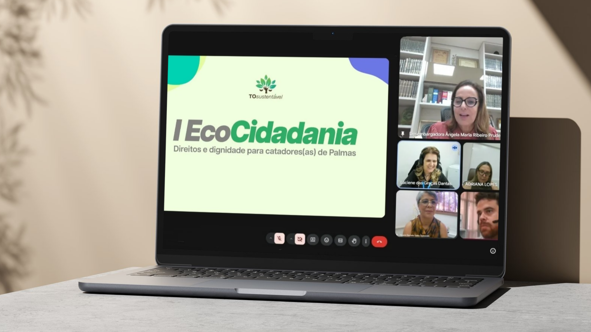 A imagem mostra um notebook sobre uma mesa exibindo uma reunião virtual do I Ecocidadania – Direitos e Dignidade para Catadores(as) de Palmas, com apresentação institucional na tela.À direita, participantes aparecem em janelas de videoconferência.