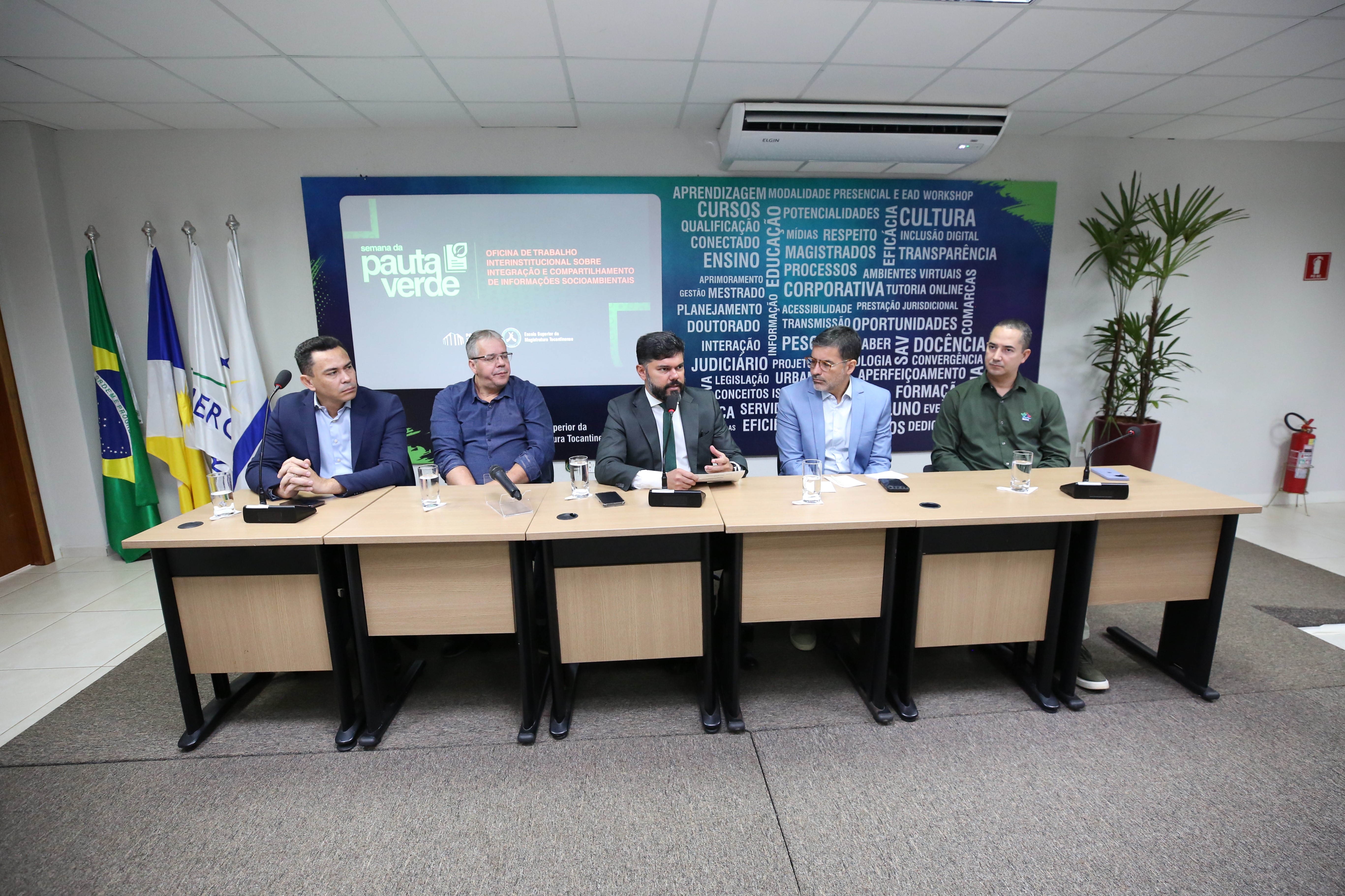 Cinco representantes participam de oficina da Semana da Pauta Verde, sentados em mesa institucional, com painel temático ao fundo e bandeiras do Brasil e do Tocantins