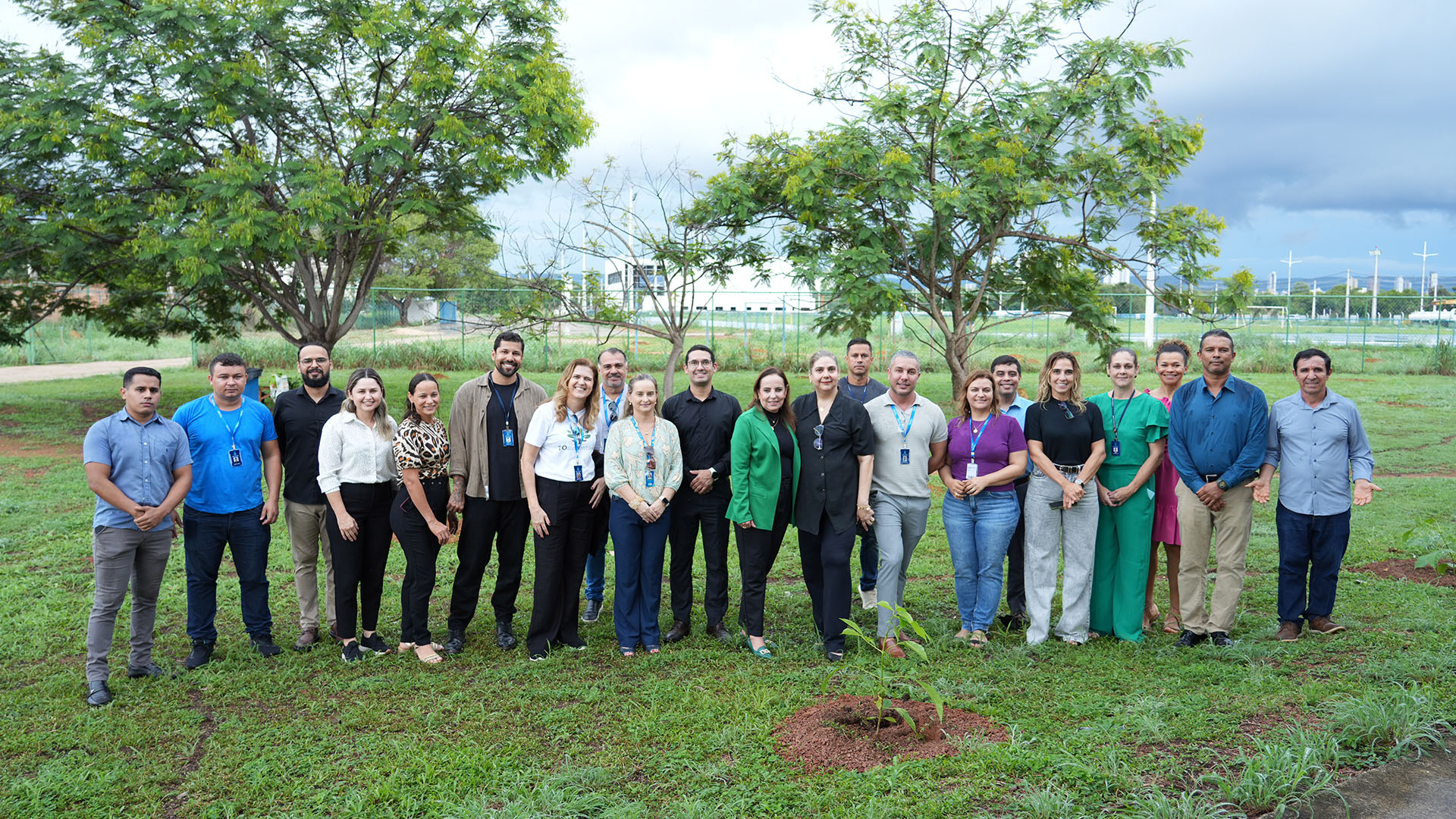 A imagem mostra um grupo de pessoas reunidas ao ar livre, na Universidade Federal do Tocantins (UFT), durante uma ação do projeto Plantar para ComPENSAR do TJTO. À frente, a árvore recém-plantada simboliza o compromisso coletivo com a sustentabilidade e a preservação ambiental.