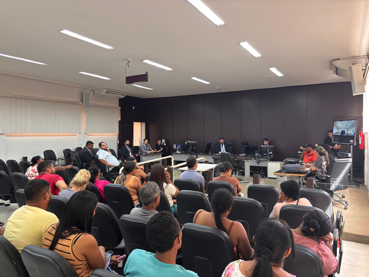 Imagem de um auditório lotado de pessoas participando de uma reunião de alinhamento; ao fundo o juiz Wellinton está sentado em uma mesa