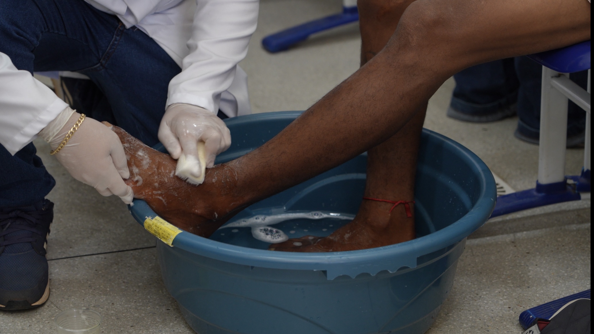 Imagem mostra mãos de estudante de medicina lavando os pés de uma pessoa em uma bacia