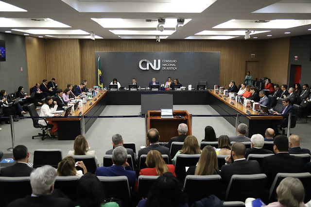 Grande número de pessoas presentes em um ambiente amplo e bem iluminado. Ao centro, na parte frontal, há um painel com a sigla “CNJ” e a frase “Conselho Nacional de Justiça”.