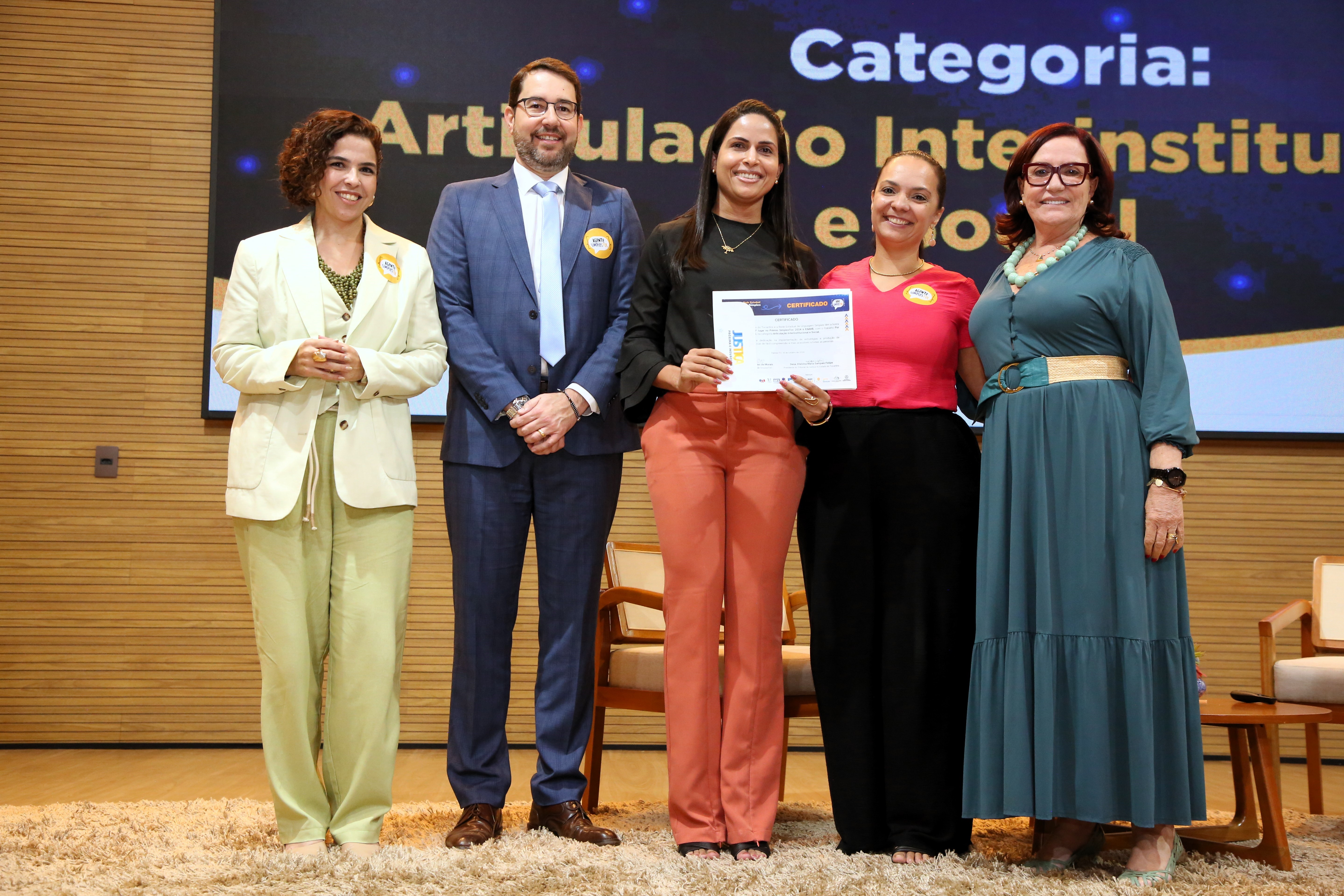 Cinco pessoas em um cenário formal posando para foto em um palco segurando um certificado