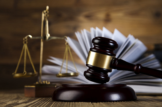 Fotografia colorida que mostra um martelo sendo batido com a imagem de uma balança da justiça atrás