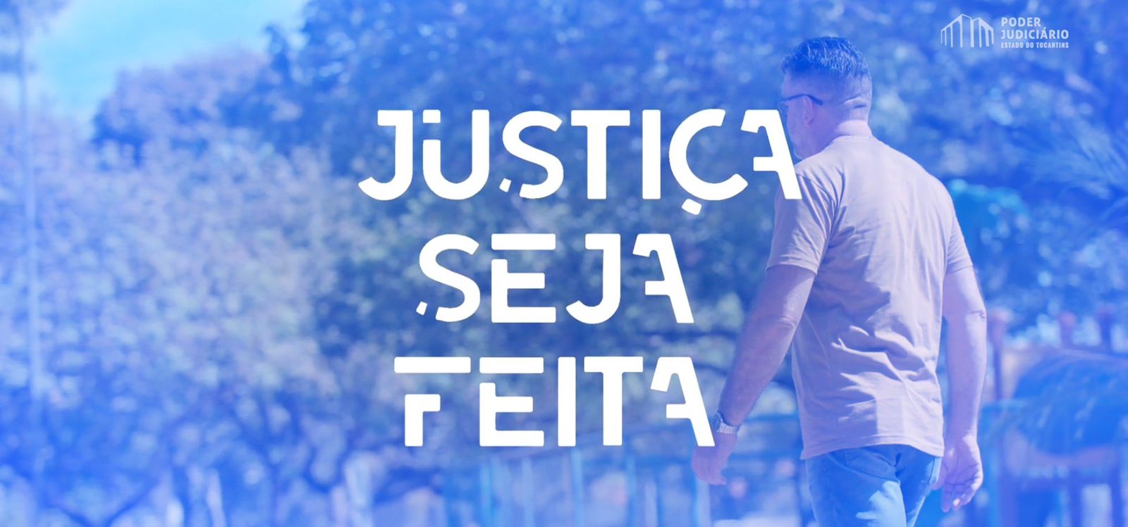 A imagem mostra um homem caminhando em um parque ensolarado. O homem está de costas para a câmera, usando uma camiseta bege e jeans azul. O fundo é desfocado, mas é possível ver árvores e um céu azul claro. Sobre a imagem, em letras brancas grandes, estão as palavras "JUSTIÇA SEJA FEITA". No canto superior direito, há um logotipo com as palavras "PODER JUDICIÁRIO ESTADO DO TOCANTINS". A imagem toda tem um tom azul.