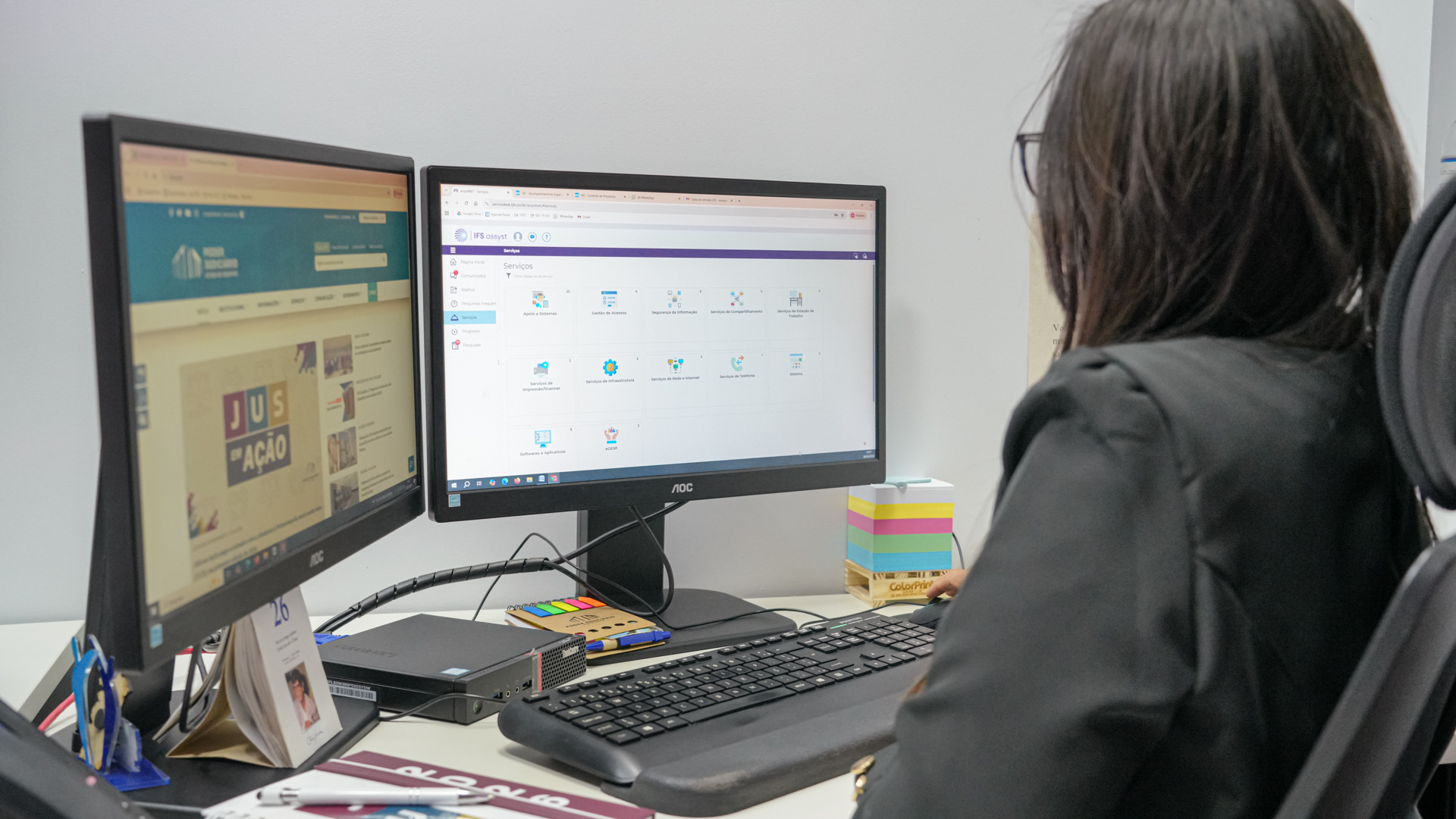 Servidora do Poder Judiciário utiliza dois monitores em estação de trabalho, acessando sistema de serviços de tecnologia da informação, em ambiente interno de escritório