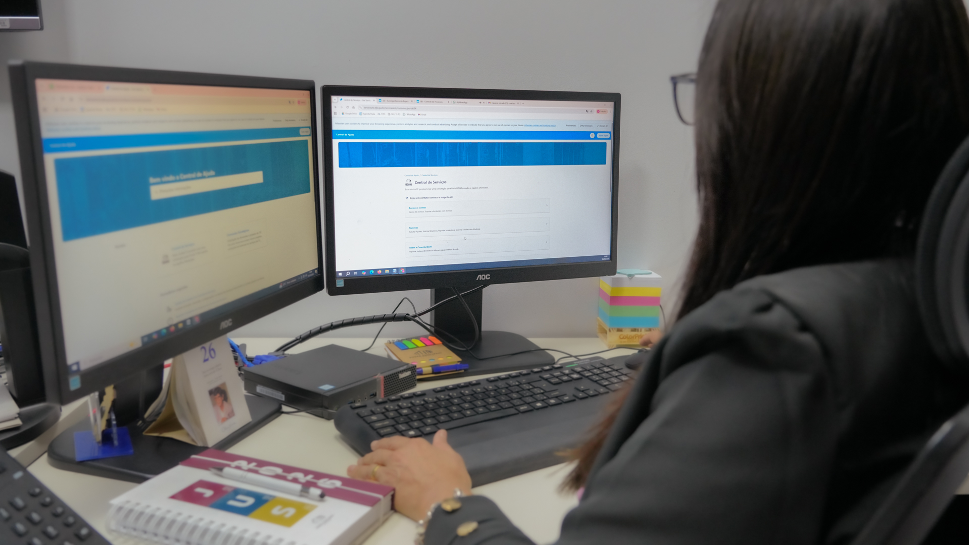 Servidora do Poder Judiciário utiliza dois monitores em estação de trabalho, acessando sistema de serviços de tecnologia da informação, em ambiente interno de escritório