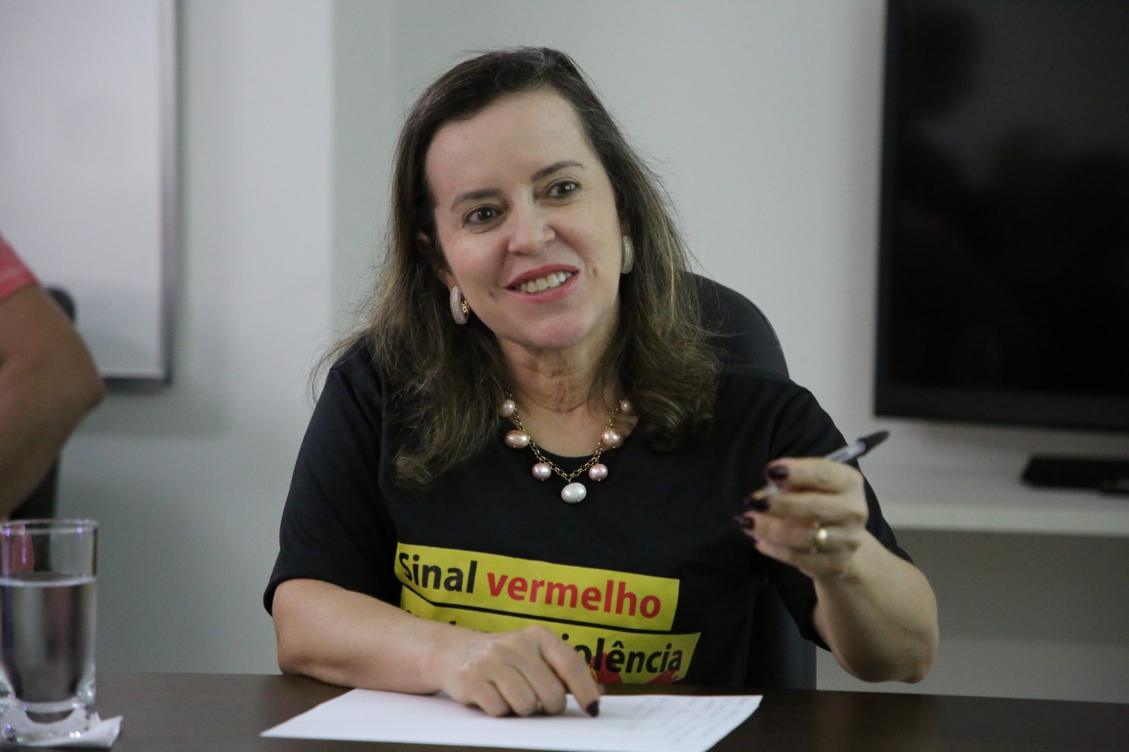 Foto de uma mulher segurando caneta e com papel sobre a mesa