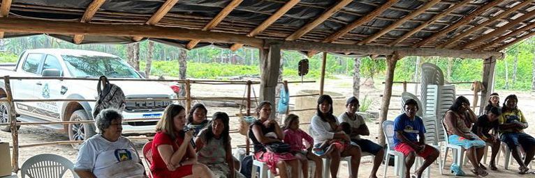 juíza Luciana conversando com indígenas; ela veste vestido vermelho e fala ao microfone