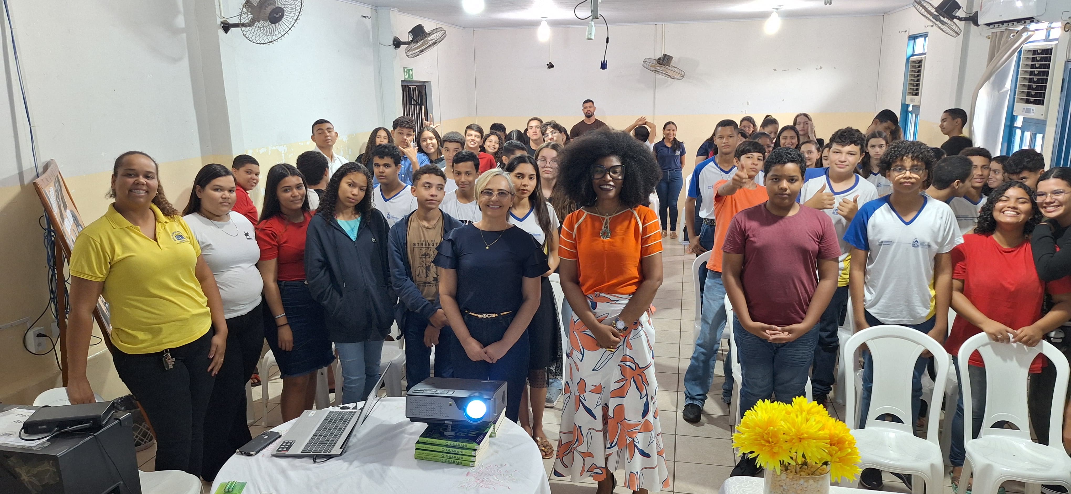 Vários alunos e professores juntos com a juíza Renata, à frente. Todos em pé, em uma sala, durante palestra sobre consciência negra