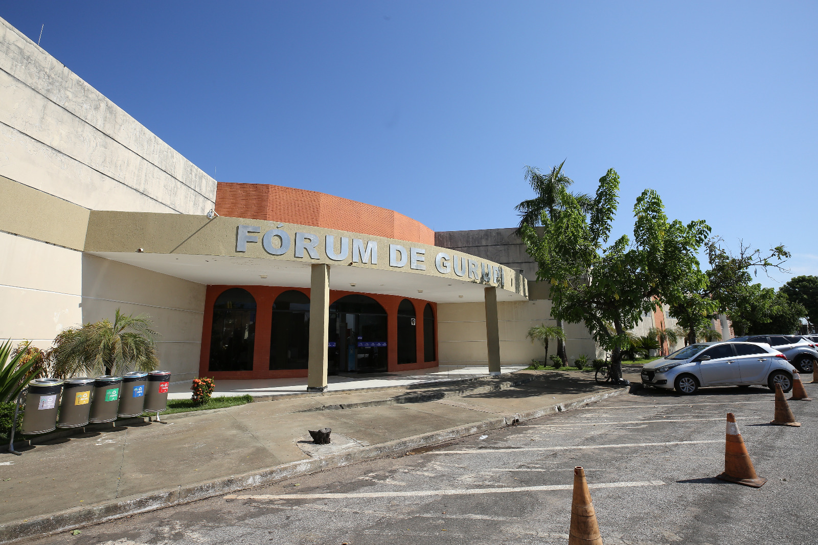 Fachada do fórum de Gurupi com parte do estacionamento à frente, com a visão das colunas, fachada ocre com letreiros prata e teto alaranjado