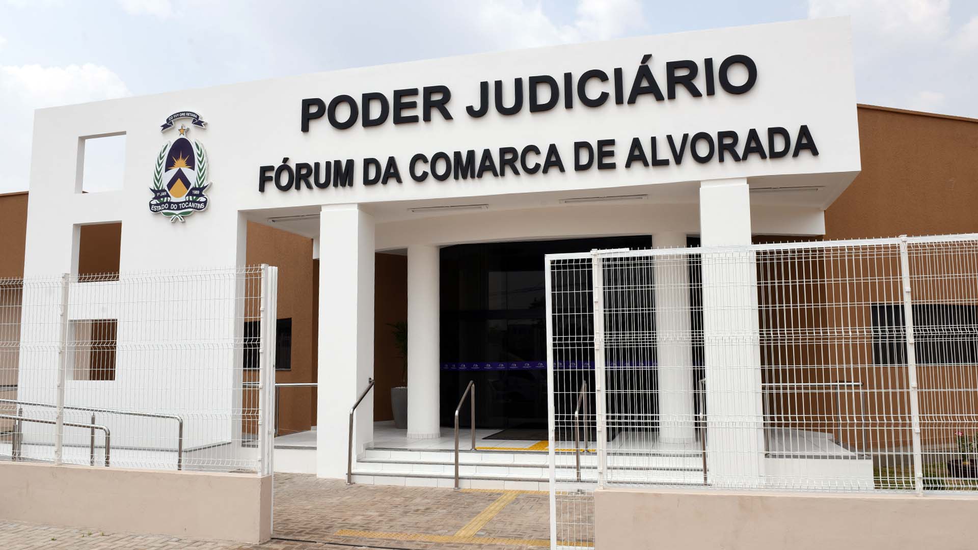 Imagem da fachada do prédio do fórum da comarca de Alvorada, prédio nas cores branca e marrom, com o nome "Poder Judiciário", Fórum da Comarca de Alvorada