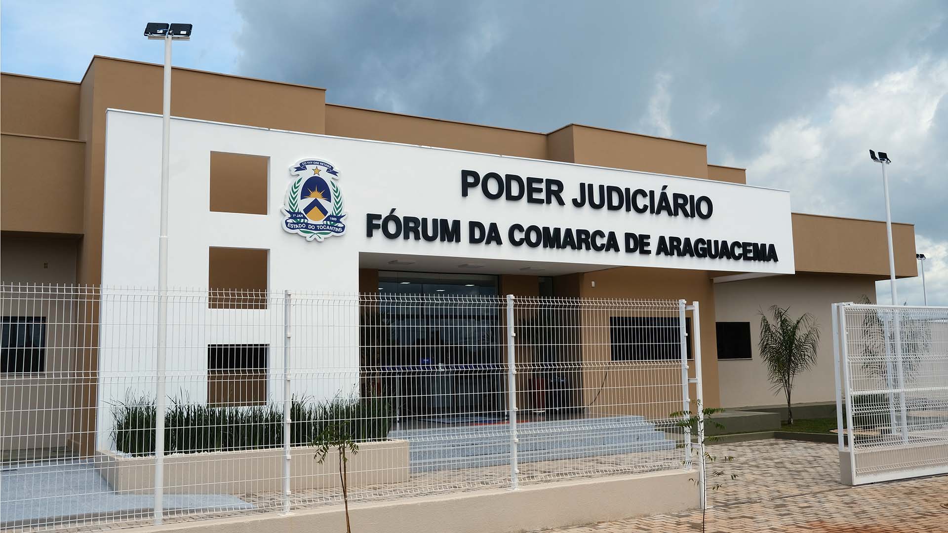 Fotografia colorida da fachada do Fórum da Comarca de Araguacema, com uma grade branca em sua frente servindo como muro 