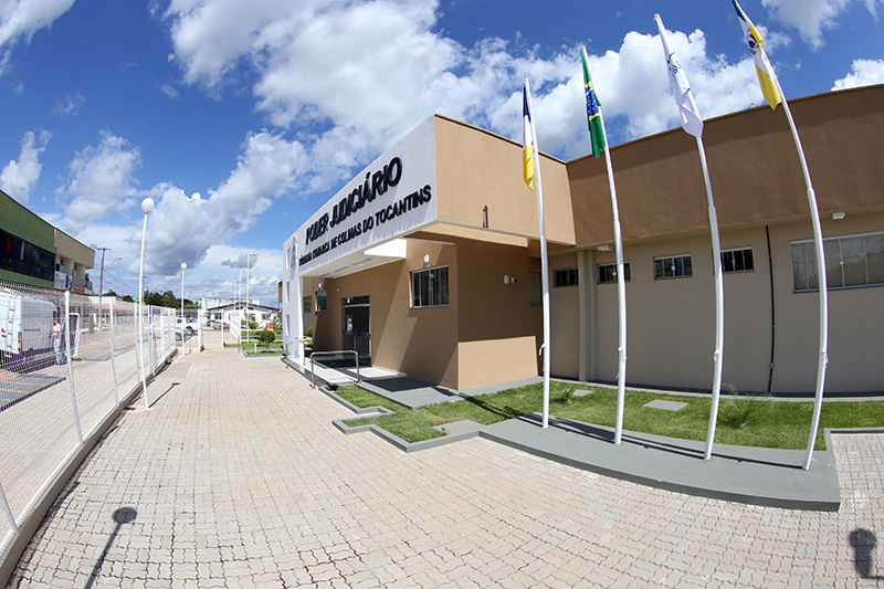 Detalhe da fachada do Fórum de Colinas, vista da lateral, com parte do pátio, mastro de bandeira, paredes na cor marrom com o pórtico contendo nome do fórum em letras pretas