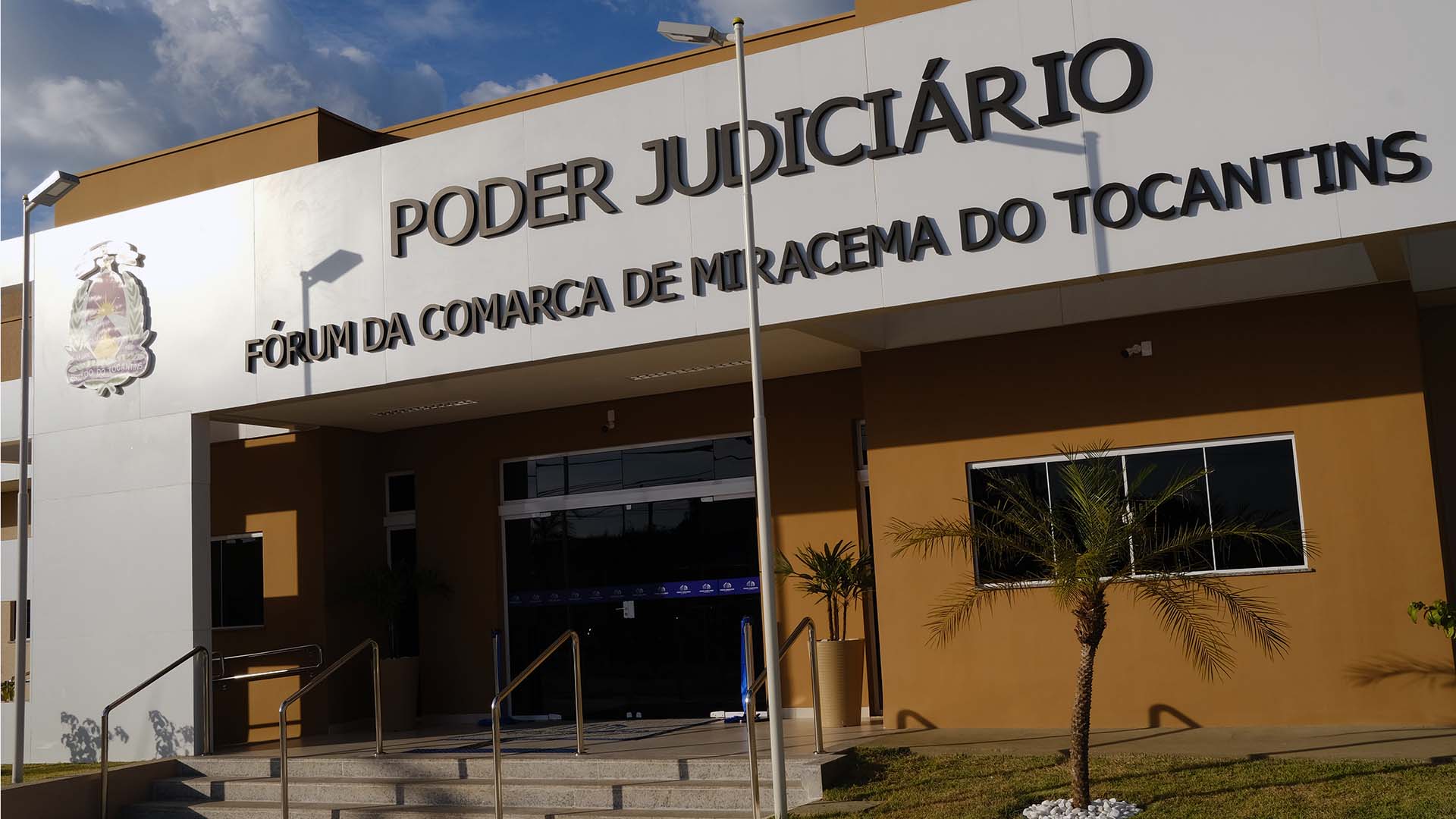 Fachada frontal na cor branca e o nome da comarca de Miracema, com a visão das colunas de sustentação e escadas de acesso