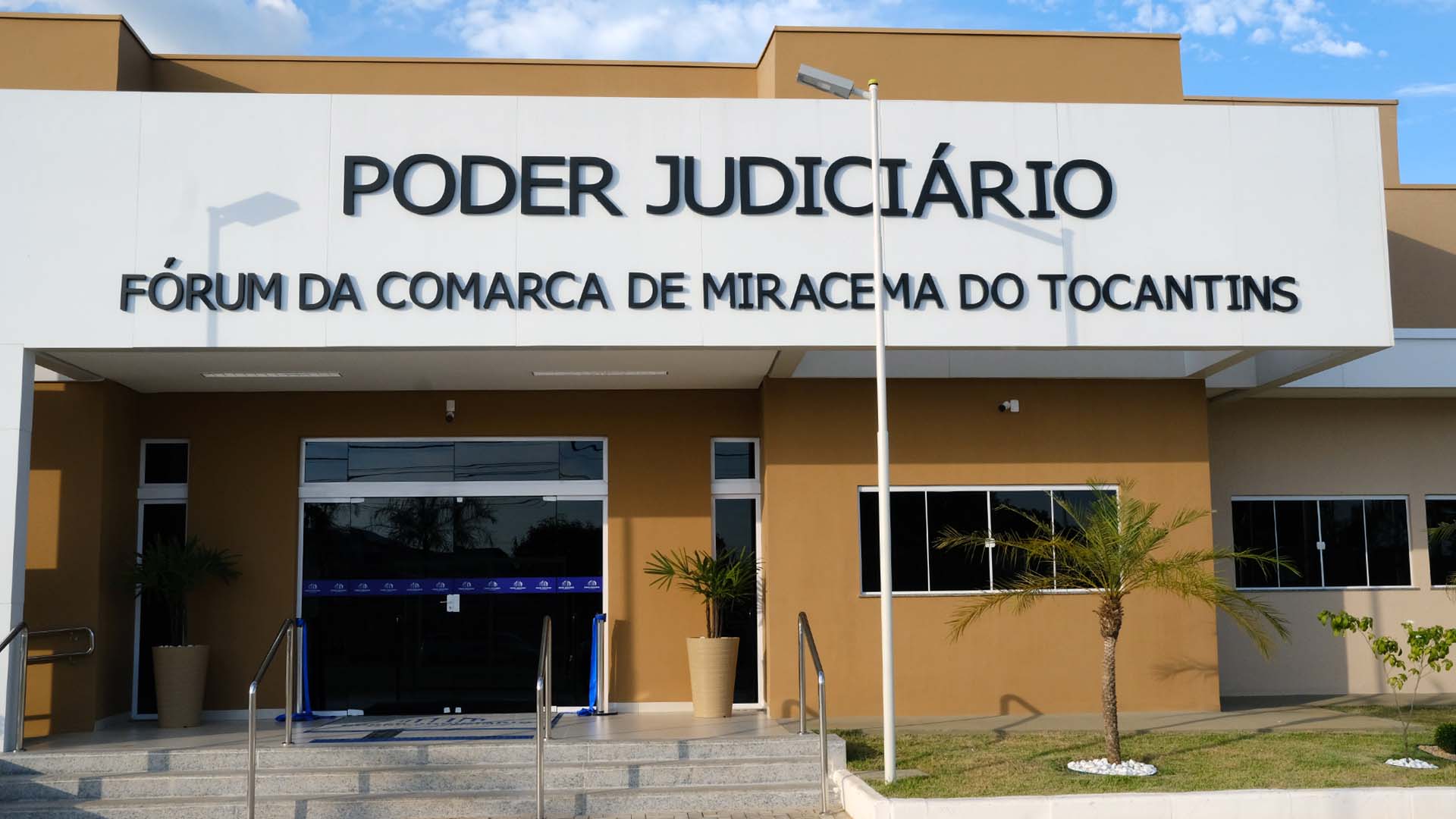 Fachada frontal na cor branca e o nome da comarca de Miracema, com a visão da escada de acesso e portas de vidro