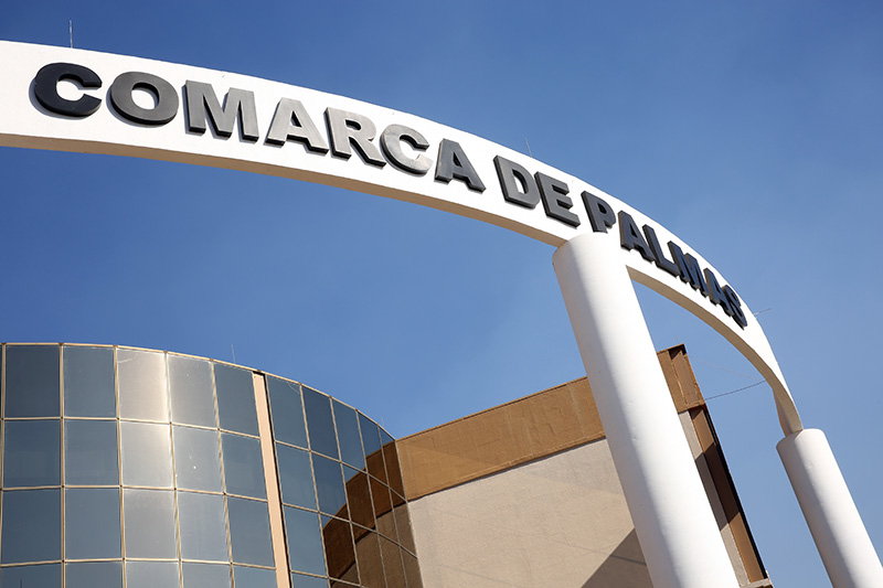 Detalhe da fachada espelhada do Fórum de Palmas mostrando recorte do pórtico branco e letreiro na cor preta