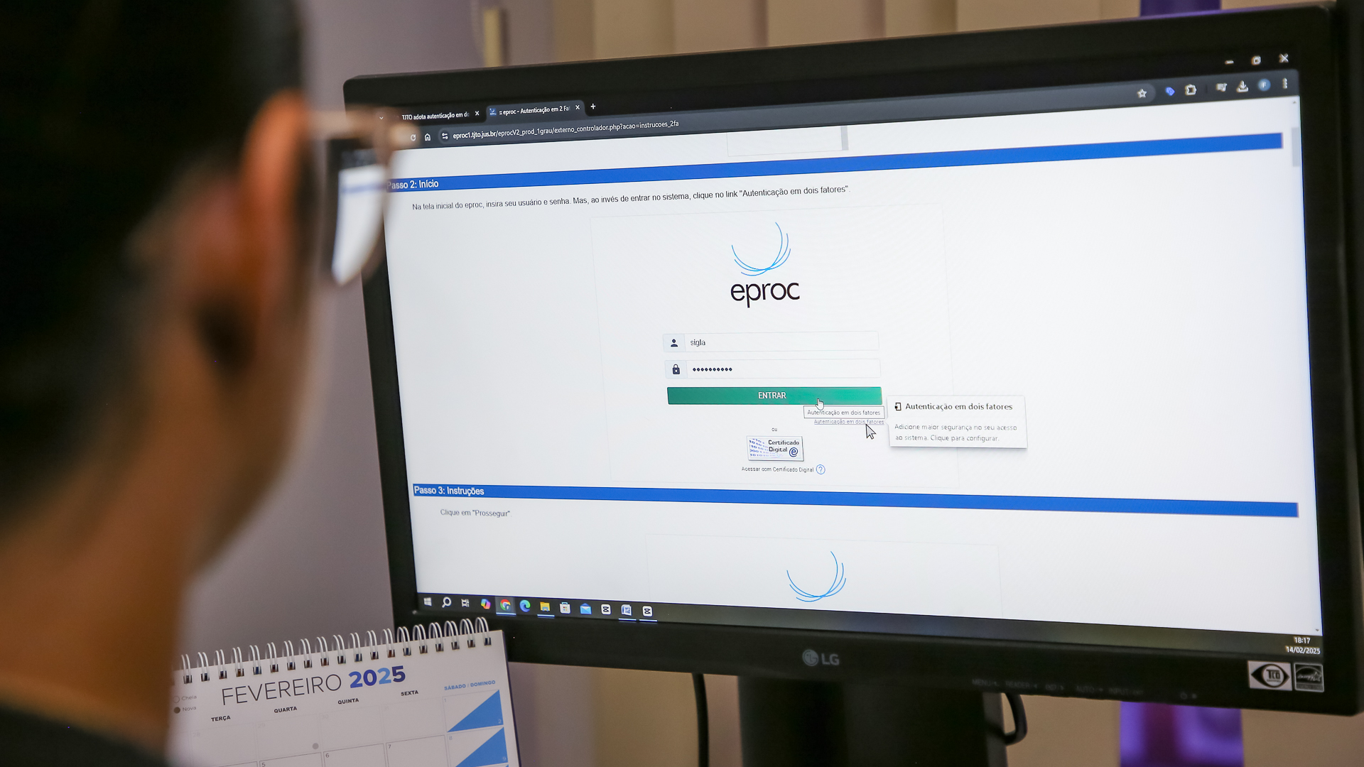 Imagem de uma tela de computador em primeiro plano com a imagem da página de acesso ao eproc projetada e o detalhe da cabeça de uma pessoa olhando a tela e fazendo o acesso