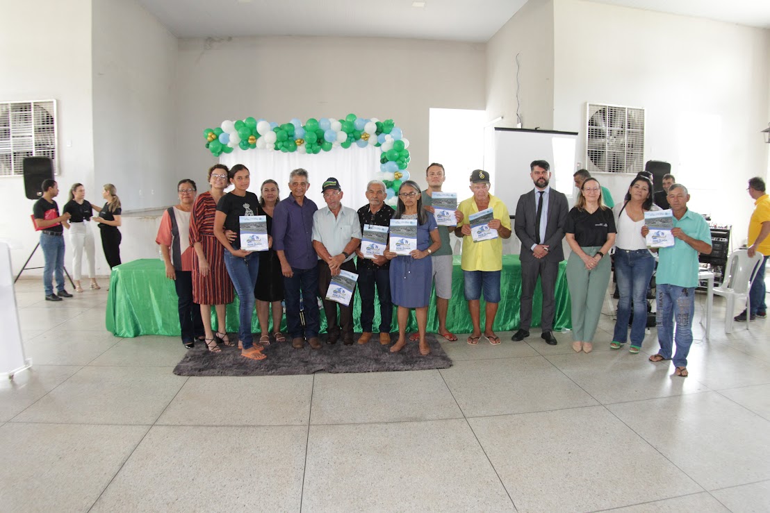 Pessoas posam para foto em auditório de paredes e piso brancas algumas seguram documentos