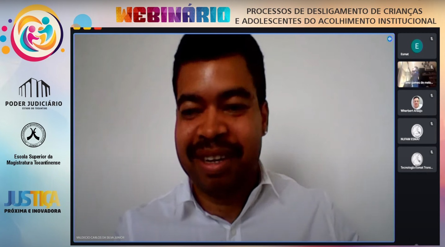 Print de uma palestra que em destaques está um participante que sorri e aparece na tela principal, a esquerda, as logos do TJTO e da Esmat. 