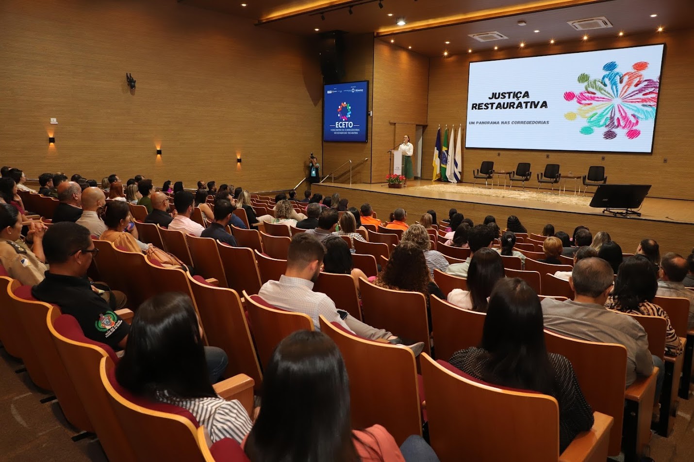 Muitas pessoas reunidas em um auditório, sentadas voltadas para o palco e atentas.