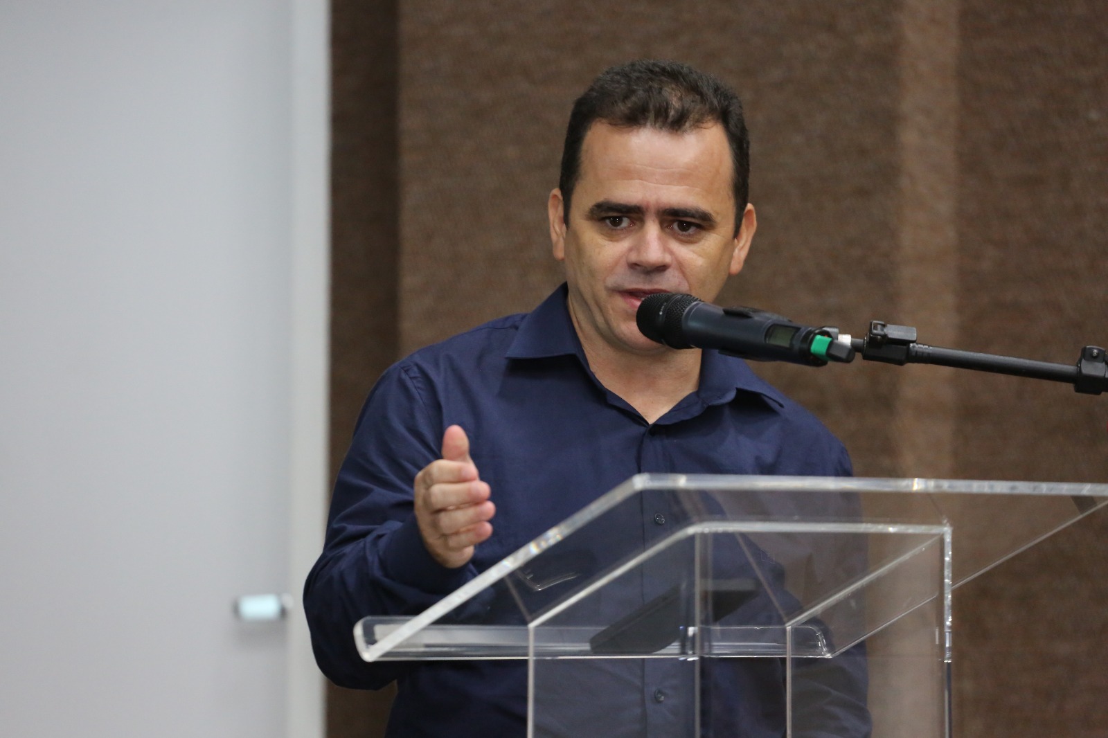 Homem calvo com cabelo preto e blusa social preta fala ao microfone