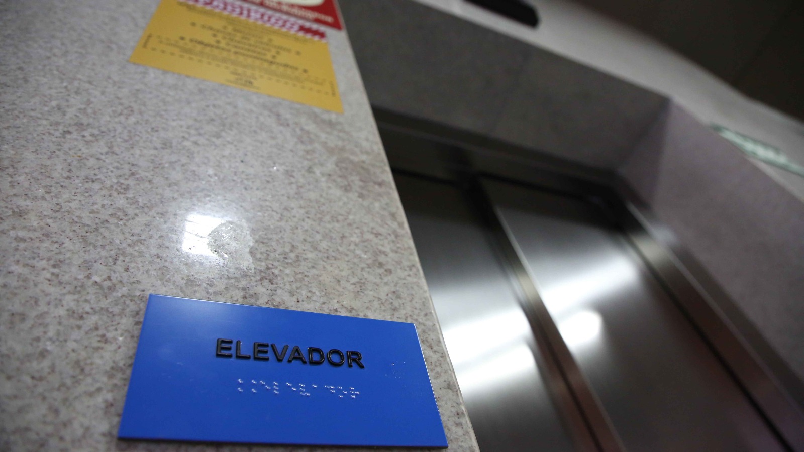 Entrada de um elevador com uma placa em braille em azul