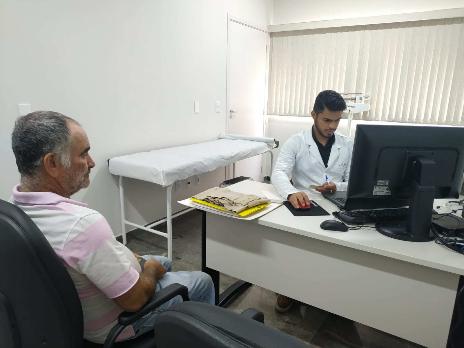 Senhor de camisa branca com detalhes rosa é atendido por servidor de jaleco branco