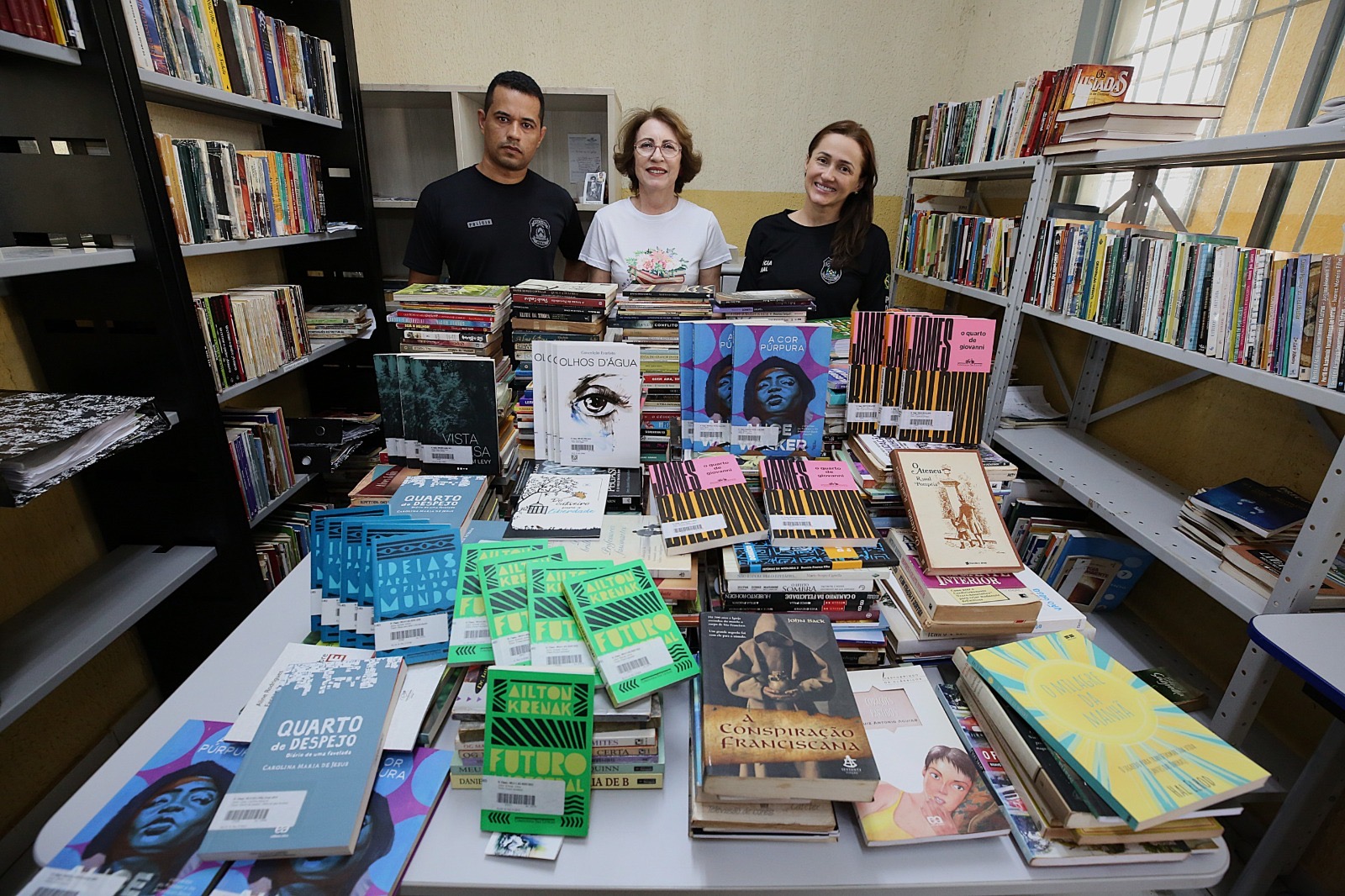 Três pessoas posando para a foto em uma sala repleta de livros variados.