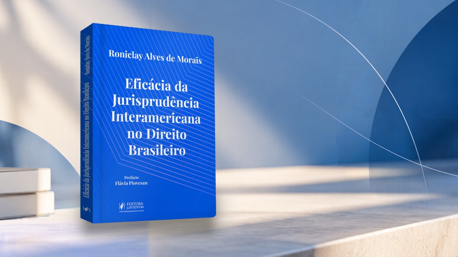 Imagem mostra capa do livro em pé sobre uma bancada e fundo nas cores azul escuro, branco e azul claro