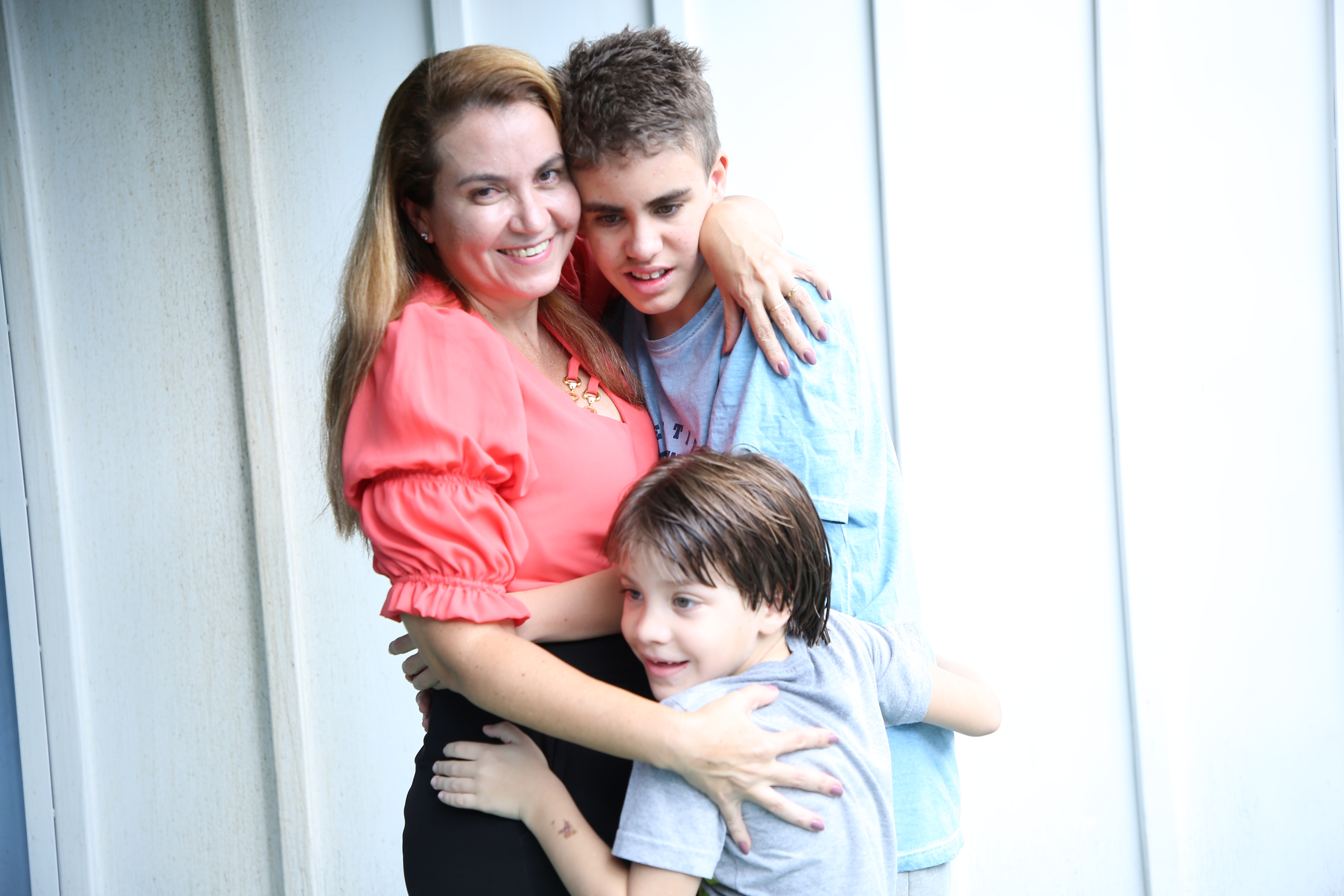 Rosa, de blusa vermelha abraçada com os filhos Heitor e Otávio, ambos com camisas azuis