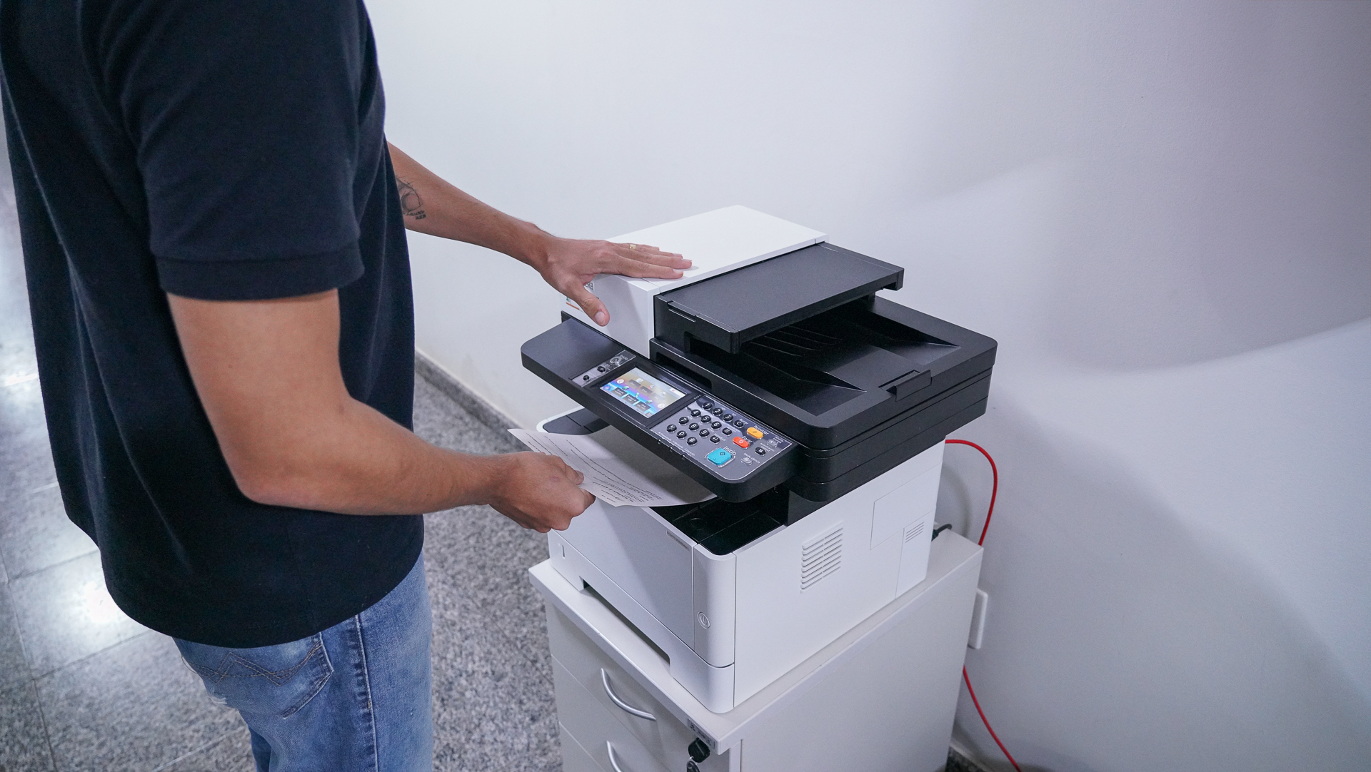 Imagem ilustrativa de uma pessoa do sexo masculino vestido de preto manuseando um equipamento de impressão