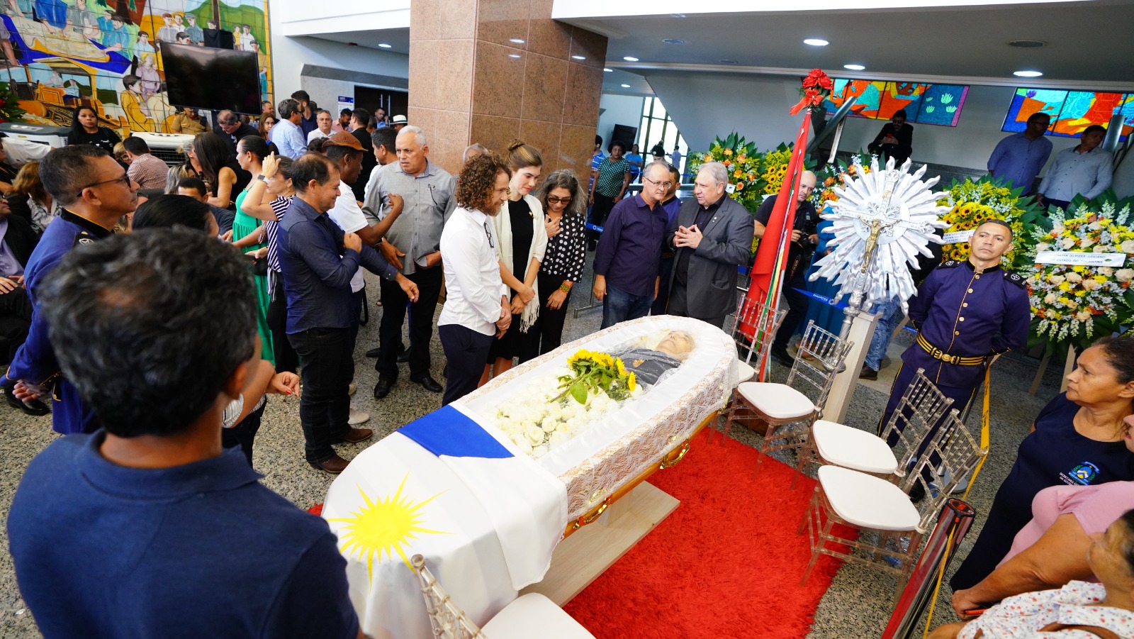 juiz Océlio Nobre ao lado do caixão de Siqueira Campos no Palácio Araguaia. Em volta, cadeiras e pessoas que foram prestar homenagens e coroas de flores