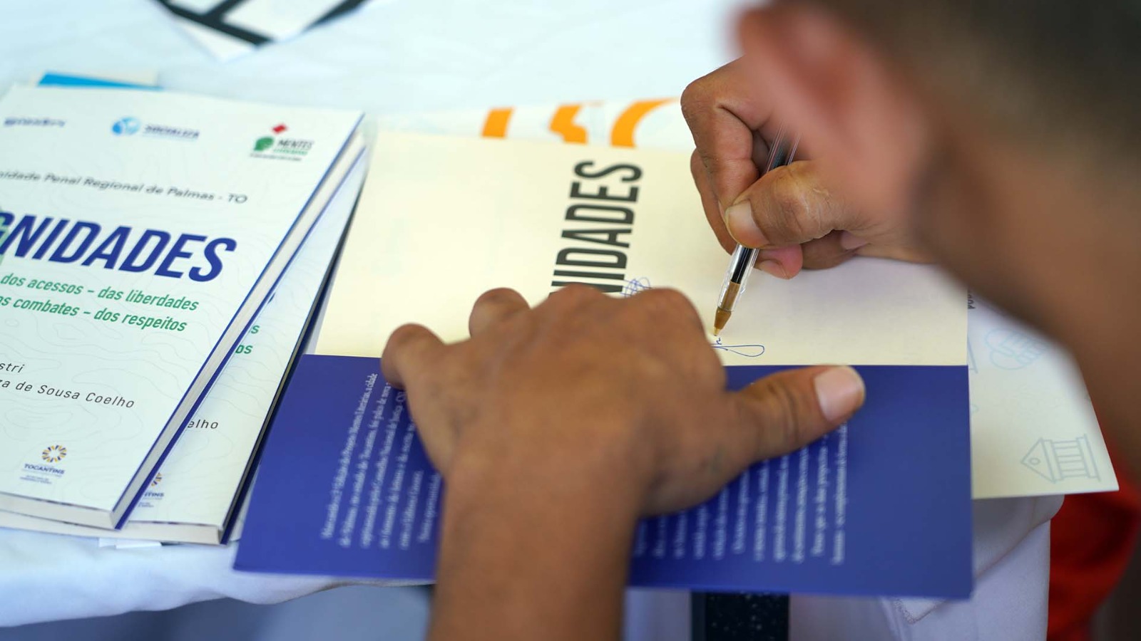 na imagem um mão autografando um livro 