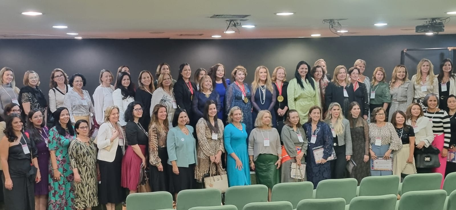 Imagem mostra um grupo grande de mulheres participantes do evento, posicionadas em fileiras frontais, todas sorrindo e olhando para a câmera.