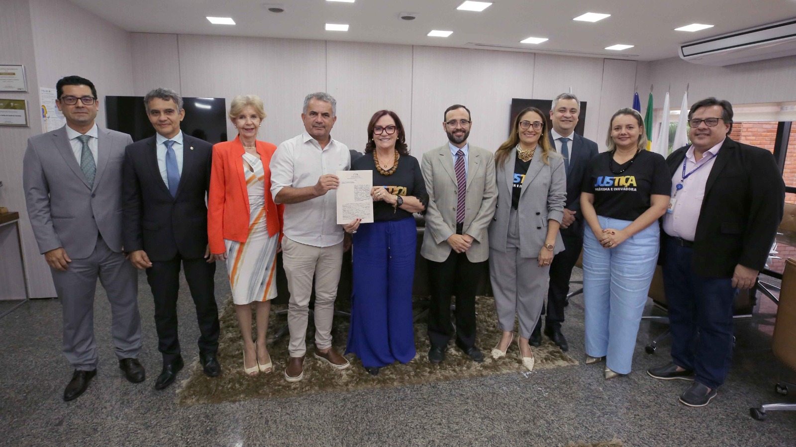 Desembargadora Etelvina ao centro segurando termo assinado ao lado de magistrados e autoridades representantes de instituições parceiras