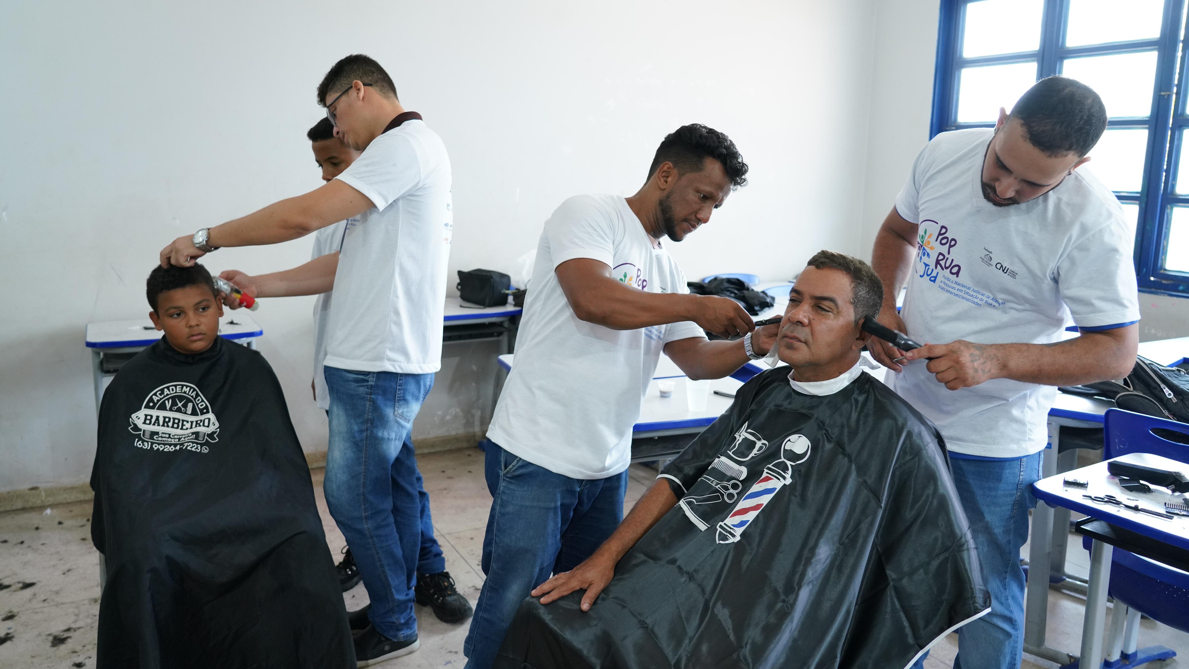 Duas pessoas recebendo atendimento de corte de cabelos por três voluntários 