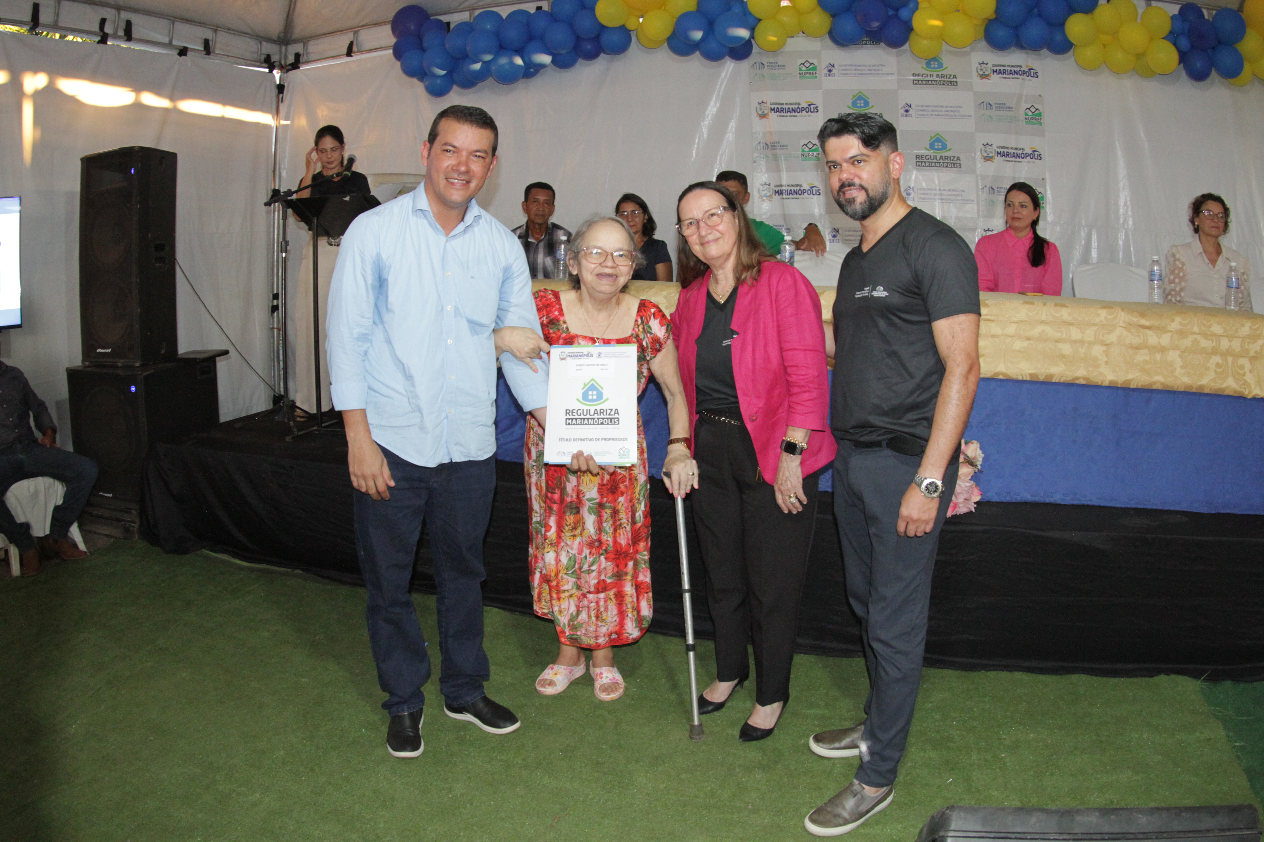 Pessoas posam para foto, uma senhora segura um documento ao centro e outras três sorriem para a foto